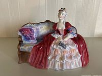 Full front view of Royal Doulton Bell O The Ball figurine showing lady in red and white gown seated on purple-upholstered antique couch