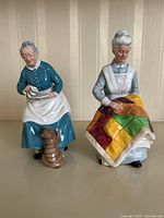 Front view showing both Royal Doulton figurines side by side on plain surface with striped wallpaper background.