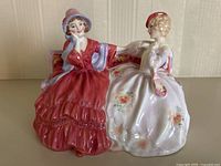 Frontal shot showing full figurine of two women seated on a bench, highlighting dresses and posture