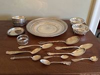 Overview of all lot items on wood surface: tray, coasters, dishes, napkin ring and spoons
