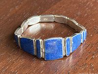 Photo of blue lapis lazuli stones set in 950 sterling silver links on the bracelet against a wood surface showing overall design and condition.