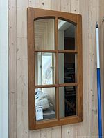 Full view of the vintage solid wood window pane mirror mounted on a wood-paneled wall, showing its overall design and structure.