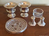 Full lot view showing two miniature urns, salt and pepper shakers, crystal coaster, and small crystal dish arranged on surface.