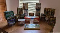 Wide shot of assorted decorative German cookie tins in various shapes and sizes on a wooden table by window blinds.