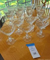 Photo showing 14 crystal stemware glasses on a wooden table with natural light. 8 taller wine glasses and 6 shorter champagne glasses are visible with detailed cut glass designs.