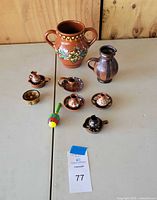 Photo of assortment of miniature clay vases and small dishes arranged on table including two vases, seven dishes, bird figurine, and wooden toy.