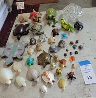 Top-down view of entire assortment of approximately 40 decorative turtles of varied sizes, materials, and colors on a white table surface.