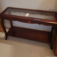 Full view of wood hall table with glass inset top, curved legs, and lower shelf.