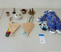 Two fabric jester dolls, two folding wooden fans, miniature copper kettle, owl figurines, trinket dish, and other small decorative items on a table.