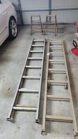 Two aluminum extension ladders and two wooden step ladders in garage with car nearby.