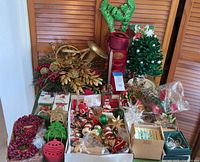 Wide shot showing entire collection of Christmas decorations on a table including headband, mailbox, artificial tree, horn centerpiece, and multiple boxed ornaments