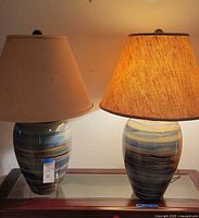 Pair of ceramic table lamps with different shades placed side by side on a glass table