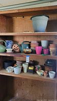 Full shelf showing a collection of assorted planter pots of varied sizes, styles, and colors including plastic, ceramic, and terracotta pots.
