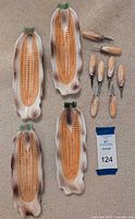 Four ceramic corn dishes and eight matching corn skewers arranged with lot number tag. Shows dish shaped like corn ears with painted detail and ceramic/skewer handles shaped like corn.