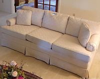 Side view of 3-seater beige sofa showing fabric upholstery, cushions, and skirted base.