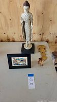 Front view of entire lot on table showing Buddha statue, Tumi figure, framed Egyptian art, and wooden camel