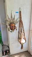 Wide view showing the clay jug hanging in macrame hanger and decorative metal mask mounted on the wall