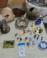 Vintage decorative items on a table including clocks, bookend, miniature figurines, sterling ashtray, and watering can.