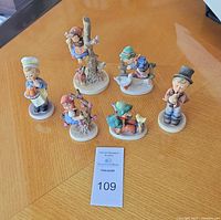 Overview of all six off-white textured vintage Goebel porcelain figurines arranged on wooden table. Each figurine depicts children in traditional styles with animals, showing detailed textured and embossed porcelain work.