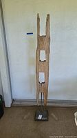 Full view of tall vertical wood fence post sculpture with natural splits and rectangular cutouts, mounted on metal base.