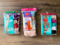 Three packages of women's underwear on wood floor including bikinis, cotton briefs by Hanes, and microfiber boy shorts in assorted colors and sizes.