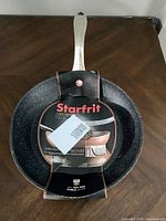 Front view of pan showing black speckled interior, copper exterior, metallic handle, and attached Starfrit Iron label.