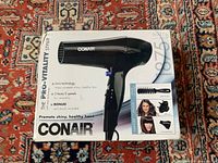 Boxed Conair Pro Vitality Styler blow dryer showing features and image of the unit and vent brush attachment on a patterned carpet background.