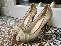 Pair of beige Christian Louboutin heels with ruched satin upper, peep-toe front, and red soles.