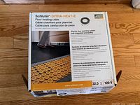 Photo of product box showing Schluter-DITRA-HEAT-E branding and product info for electric floor heating cable system with integrated uncoupling.