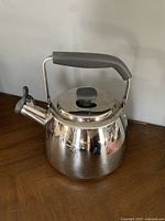 Full view of stainless steel whistling tea kettle showing black handle and spout lever.