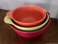 View of three nested plastic mixing bowls in orange, green, and pink, showing their sizes and colors.