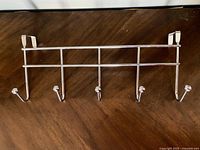 Photo showing white metal over door hanger with five hooks on wooden surface.