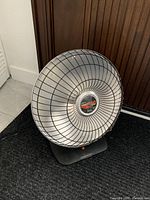 Front view of the parabolic heater showing the metal grill and base with power button and indicator light.