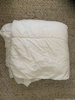 Folded white queen size duvet on carpeted floor.