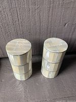 Two cylindrical salt and pepper shakers made from mother of pearl shell, standing upright showing top and side views.