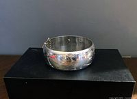 Front view of wide silver bangle bracelet showing engraved floral and leaf pattern