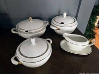 Three covered serving bowls and a gravy boat with underplate, displayed on a table.