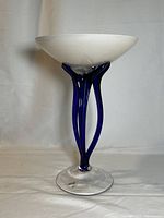 Front view of the art glass pedestal bowl vase showing white bowl top, cobalt blue stems, and clear base with label.
