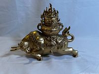 Side view of brass bull figurine showing the detailed urn with flame motifs on the back and coin necklace decorations.