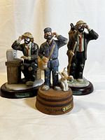 Front view of three Flambro Emmett Kelly Jr clown porcelain figurines arranged on wooden stands with labels.
