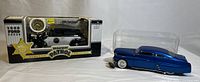 Photo showing both die cast cars: a black and white 1940 Ford Sedan California Highway Patrol model in original box, and a blue 1949 Ford Mercury model in plastic display case.