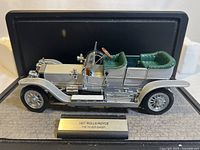 Side view of 1:24 scale Franklin Mint diecast model of the 1907 Rolls Royce Silver Ghost showing silver body with green interior and detailed wheels. Mounted on a base with label.