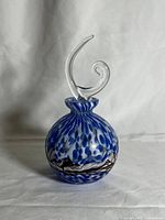 Full view of the blue and white spotted glass perfume bottle with clear whimsical curved stopper against neutral background.