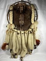 Front view of large Indigenous American dream catcher showing braided cords, fur backing, feathers and beads