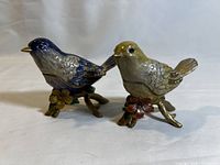 Pair of jeweled enamel bird trinket boxes, showing blue and yellow birds side by side on branches with flowers.