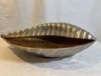 Side view of the metallic shell-shaped bowl showing the ribbed silver body and gold-toned interior.