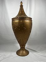 Front view of large gold ceramic vase with lid, showing full height and pedestal base.