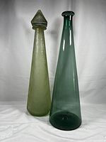 Two mid century modern green glass genie bottles; one frosted and speckled with cork stopper, the other clear green with wide rim