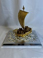 Front angle view of gold-colored Japanese treasure ship model on silver textured base, showing dragon figurehead and figures aboard.