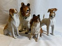 Four vintage dog figurines displayed together on a white background, showing their full front and side profiles, highlighting size and color variations.